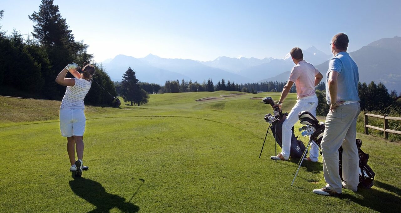 Golferinnen und Golfer auf einem Alpenplatz mit Blick auf die Bergkette.