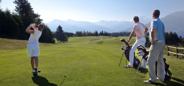 Golferinnen und Golfer auf einem Alpenplatz mit Blick auf die Bergkette.