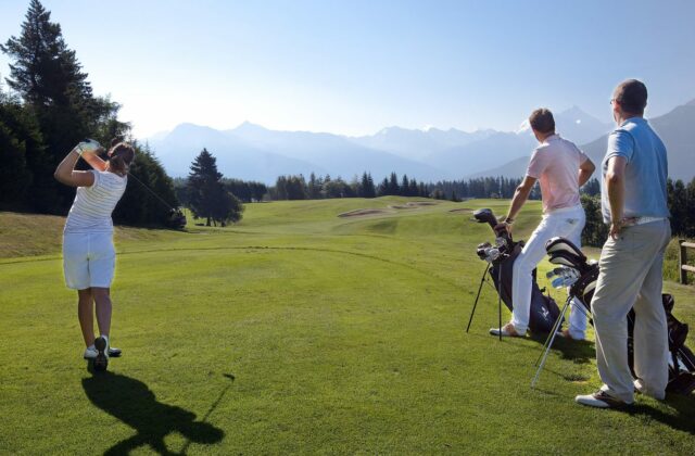 Golferinnen und Golfer auf einem Alpenplatz mit Blick auf die Bergkette.