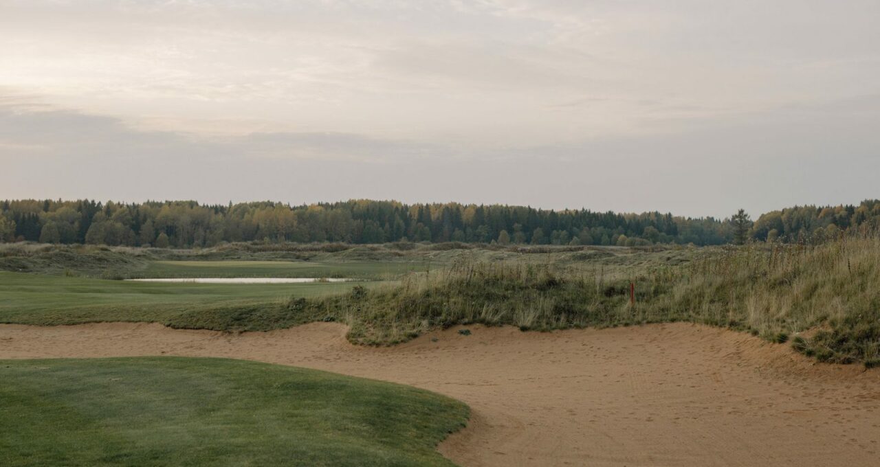 Fairway de links bordé de dunes de sable et d'herbes hautes.