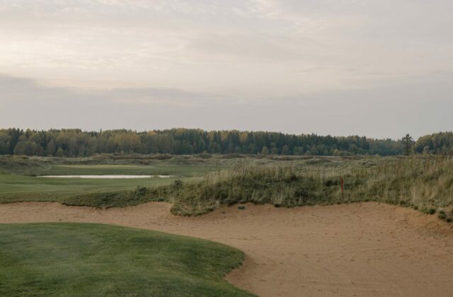 Fairway de links bordé de dunes de sable et d'herbes hautes.