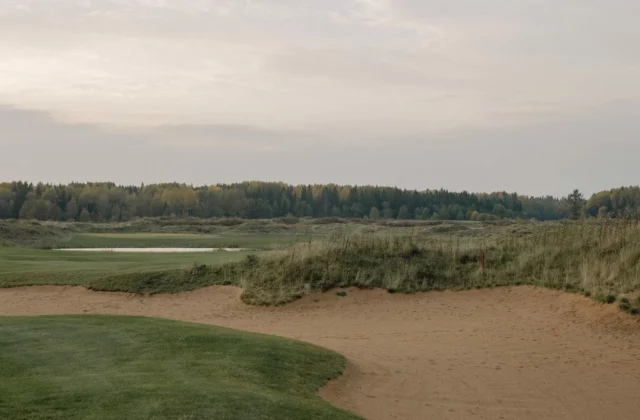 Fairway de links bordé de dunes de sable et d'herbes hautes.