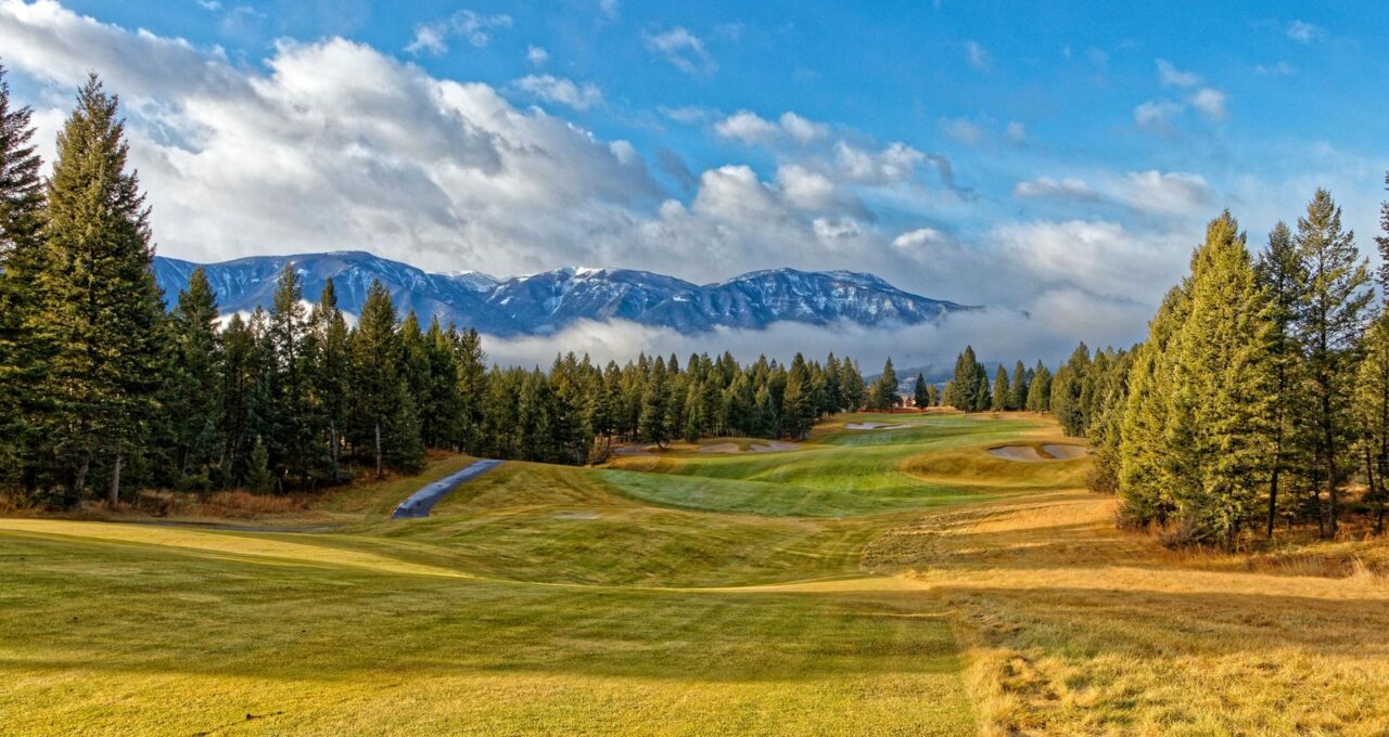 Parcours de golf de montagne, sommets enneigés et pins en arrière-plan.