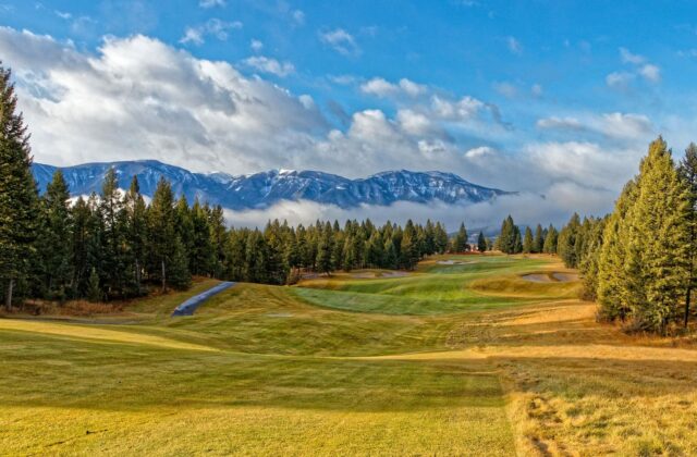 Parcours de golf de montagne, sommets enneigés et pins en arrière-plan.