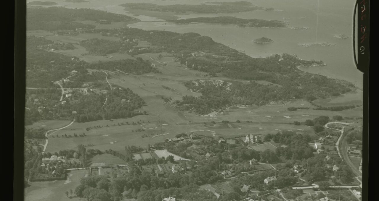 Golfbana med öppna spelfält och skog i bakgrunden.