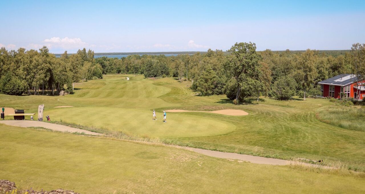 Blick über einen Golfplatz mit Grün, Bunker und Spielern.