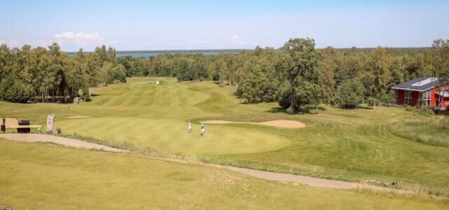 Blick über einen Golfplatz mit Grün, Bunker und Spielern.