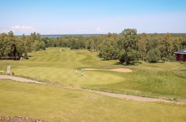 Blick über einen Golfplatz mit Grün, Bunker und Spielern.