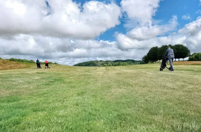 Three golfers walking up a fairway pushing their trolleys under a cloudy sky