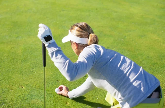 Golferin in der Hocke auf dem Grün, auf ihren Schläger gestützt, legt ihren Ball mit gebeugten Knien zurück