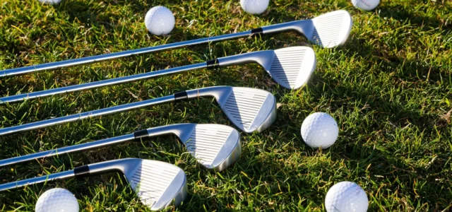 Cinq fers de golf posés côte à côte sur l'herbe, faces visibles, entourés de balles blanches
