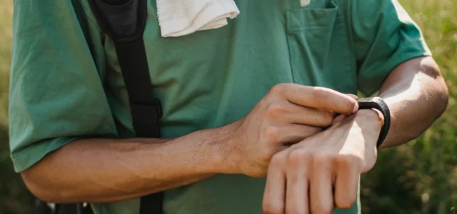 Man in a green T-shirt adjusting the smartwatch on his wrist outdoors