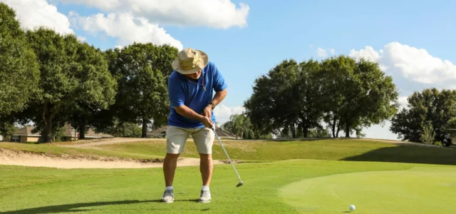 Golfer in a canvas hat and blue polo putting from the edge of the green