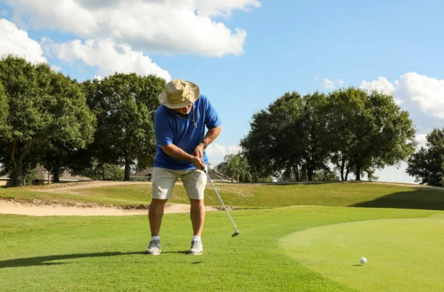 Golfer mit Stoffhut und blauem Polo puttet vom Rand des Grüns