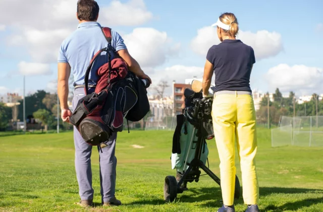 Golfer mit dem Bag auf der Schulter und Golferin mit ihrem Trolley, von hinten, mit Blick auf den Platz