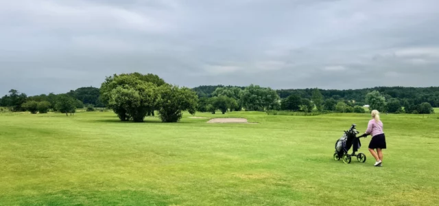 Woman golfer pushing her trolley and bag along a fairway under a cloudy sky