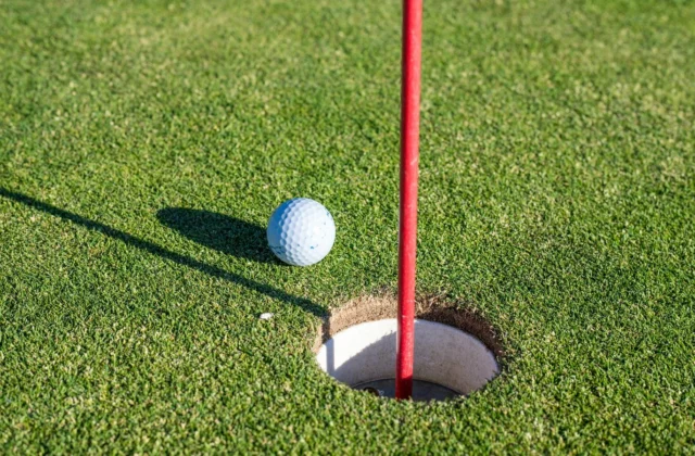 Balle de golf au bord du trou, drapeau incliné