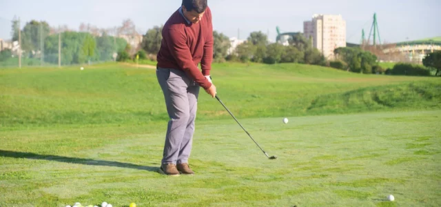 Golfeur jouant un fer sur un practice en herbe, un tas de balles à ses pieds
