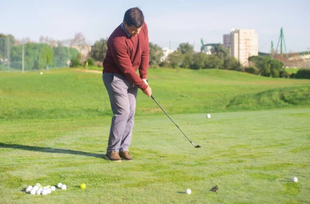 Golfer slaat een ijzer op een grasafslag van de driving range, een hoopje ballen voor hem