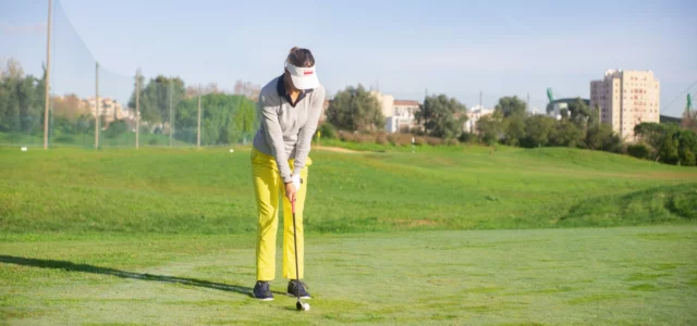 A golfer practising alone on a short-game area, a pile of balls at her feet, lining up a chip
