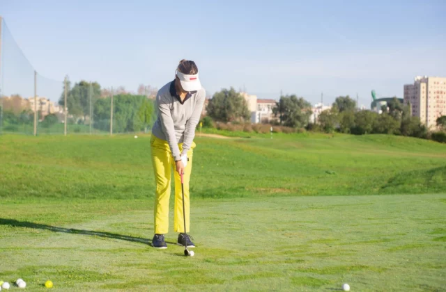 Golferin übt allein auf einer Übungsfläche, einen Haufen Bälle neben sich, und bereitet einen Chip vor