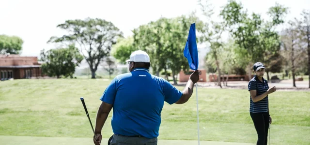 Two golfers on a green, one tending the flag