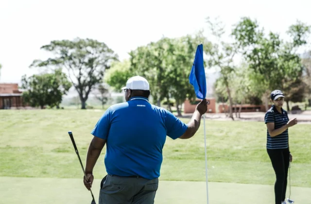 Two golfers on a green, one tending the flag