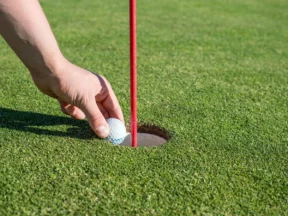 Main retirant une balle du trou, drapeau rouge en place