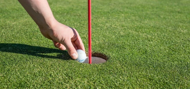 Hand lifting a ball out of the hole, red flagstick in place