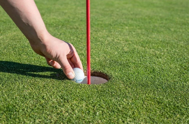Main retirant une balle du trou, drapeau rouge en place
