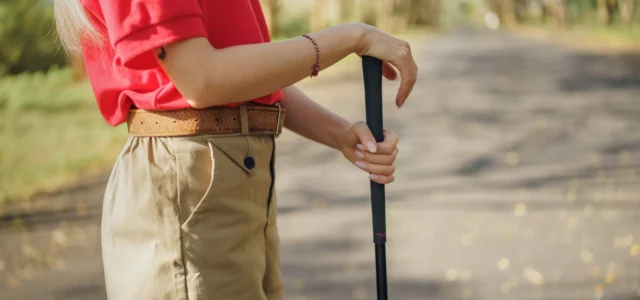 Golfer holding the black grip of an upright club with both hands on a shaded path