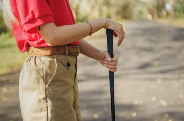Golfer holding the black grip of an upright club with both hands on a shaded path