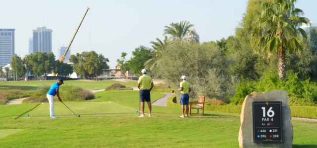 Three golfers on a tee on a sunny morning: one hits while the other two wait their turn