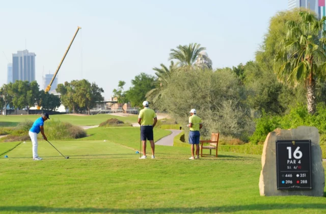 Drei Golfer auf einem Abschlag an einem sonnigen Morgen: Einer schlägt ab, die beiden anderen warten, bis sie an der Reihe sind