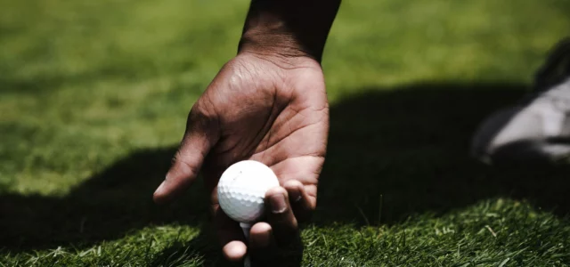 En hand sätter en golfboll på en peg i det kortklippta gräset på en tee
