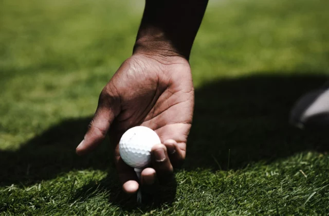 Eine Hand setzt einen Golfball auf ein Tee im kurz geschnittenen Gras eines Abschlags