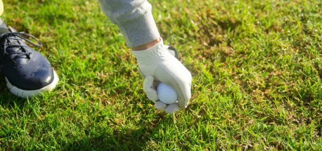 Behandschuhte Hand legt einen Ball aufs Grün