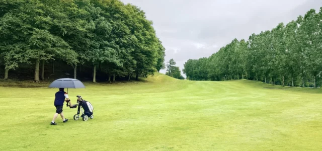 Golfers under an umbrella on a fairway