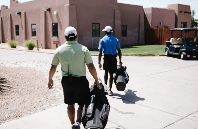 Twee golfers lopen met hun tassen naar de parkeerplaats