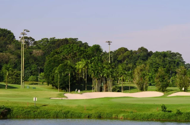Vijver op de voorgrond, rode paaltjes langs de oever, bunkers en een green erachter