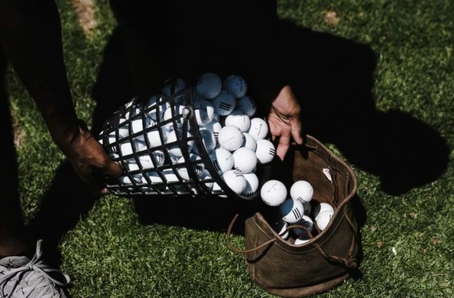 Hände schütten einen Drahtkorb voller gebrauchter Golfbälle in eine abgenutzte Ledertasche im Gras