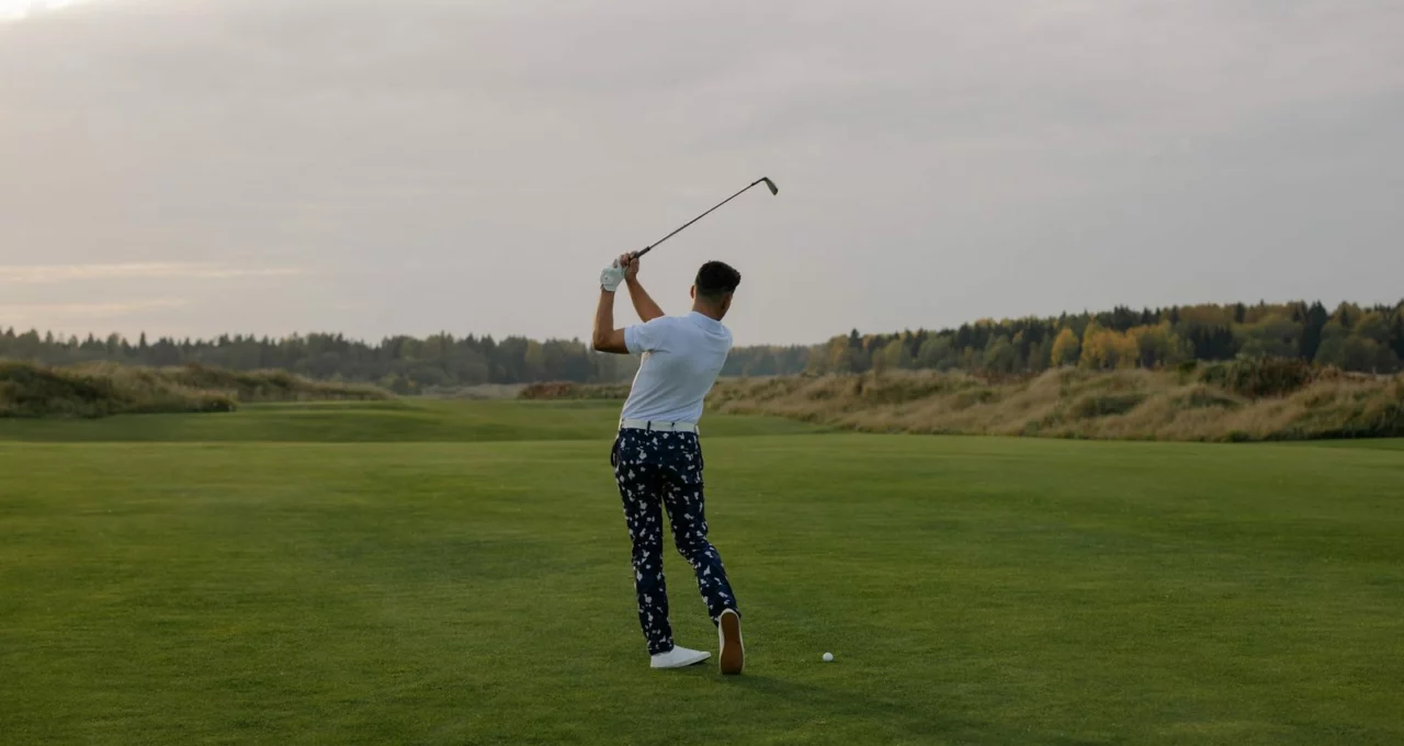 Golfeur vu de dos, un fer levé au-dessus des épaules, la balle posée sur un fairway bordé d'arbres d'automne
