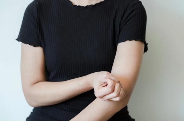 Eine Frau hält sich den Unterarm knapp unterhalb des Ellbogens