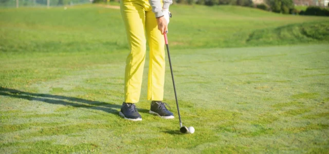 Golfeur en pantalon jaune à l'adresse avec un fer, la balle posée sur l'herbe rase d'un fairway