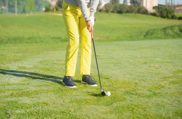 Golfer in gelber Hose bei der Ansprache mit einem Eisen, der Ball liegt auf kurz gemähtem Fairway-Gras
