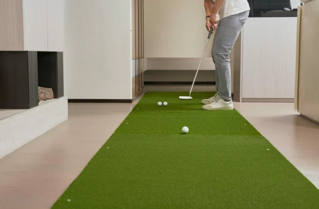 Golfer übt das Putten auf einer langen grünen Matte im Flur einer Wohnung