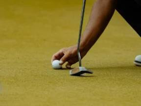 Un golfeur pose sa balle sur le green, juste devant un putter maillet tenu à la verticale