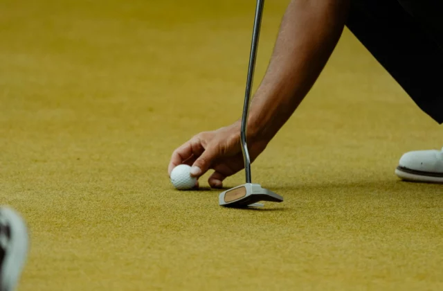 Ein Golfer legt den Ball auf dem Grün direkt vor einen senkrecht gehaltenen Mallet-Putter